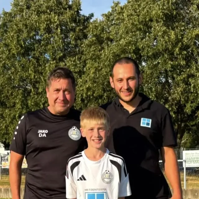 Übergabe der neuen Trikots an die D2-Junioren der JSG Mühlbachtal auf dem Sportplatz: ein Spieler im weißen Trikot mit Technik-Schneider-Logo zwischen einem Trainer und einem Vertreter von Technik-Schneider